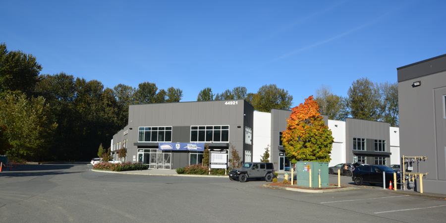 Front of 44921 Commercial Court, a two-storey grey and white tilt-up building with storefront glazing and an autumn maple tree